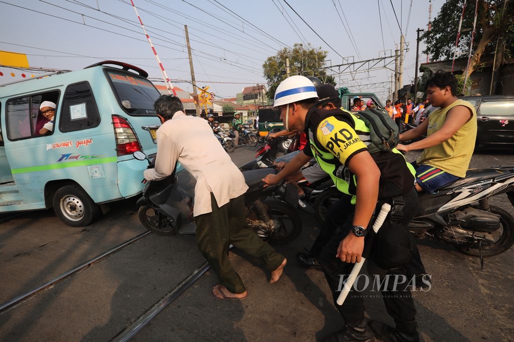 Petugas keamanan PT KAI Daop I Jakarta membantu pengendara yang motornya mogok untuk menyeberangi pelintasan sebidang Manggarai, Jakarta Selatan, Selasa (17/9/2019).