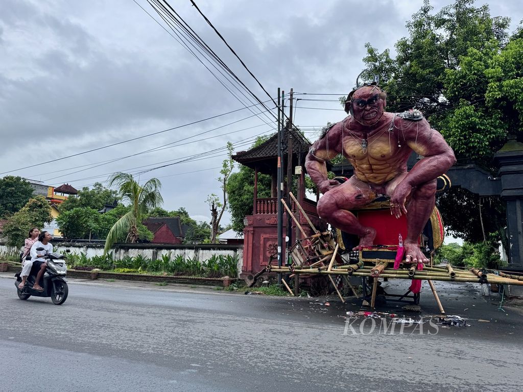 Warga melintas di depan gerbang yang ditutup dengan ogoh-ogoh saat Nyepi di salah satu lingkungan di kawasan Cakranegara, Kota Mataram, Nusa Tenggara Barat, Senin (11/3/2024).
