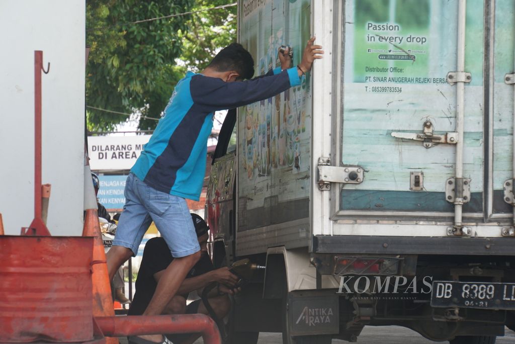 Ghery (22, kaus biru) mengguncang-guncangkan mobil pikap yang ia kendarai, sementara Andi (22), rekannya, mengisi solar ke tangki, Kamis (24/3/2022) siang, di Manado, Sulawesi Utara. Solar bersubsidi sedang langka karena setiap SPBU hanya mendapatkan kuota penyaluran sebesar 8.000 liter.