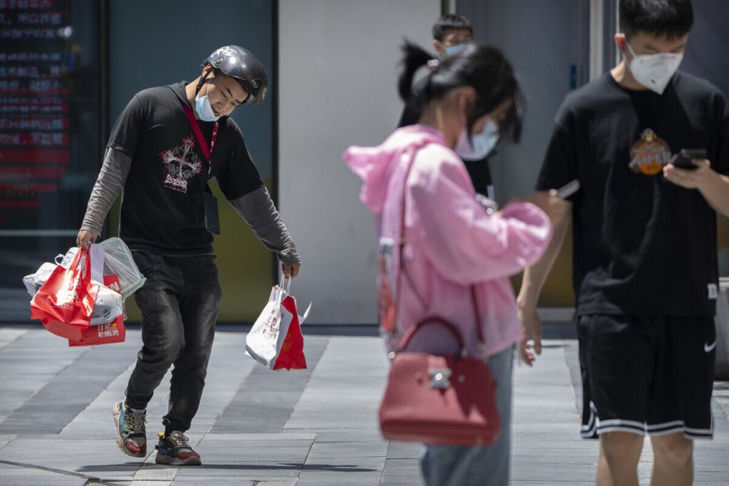 Seorang petugas jasa antar membawa pesanan berjalan melintas di pedestrian kompleks perkantoran di Beijing, Jumat (28/5/2021).