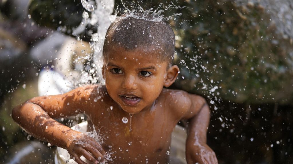 Seorang anak mandi untuk mengusir panas dengan memanfaatkan air yang keluar dari pipa bocor di pinggiran Jammu, India, Jumat (31/5/2024). 