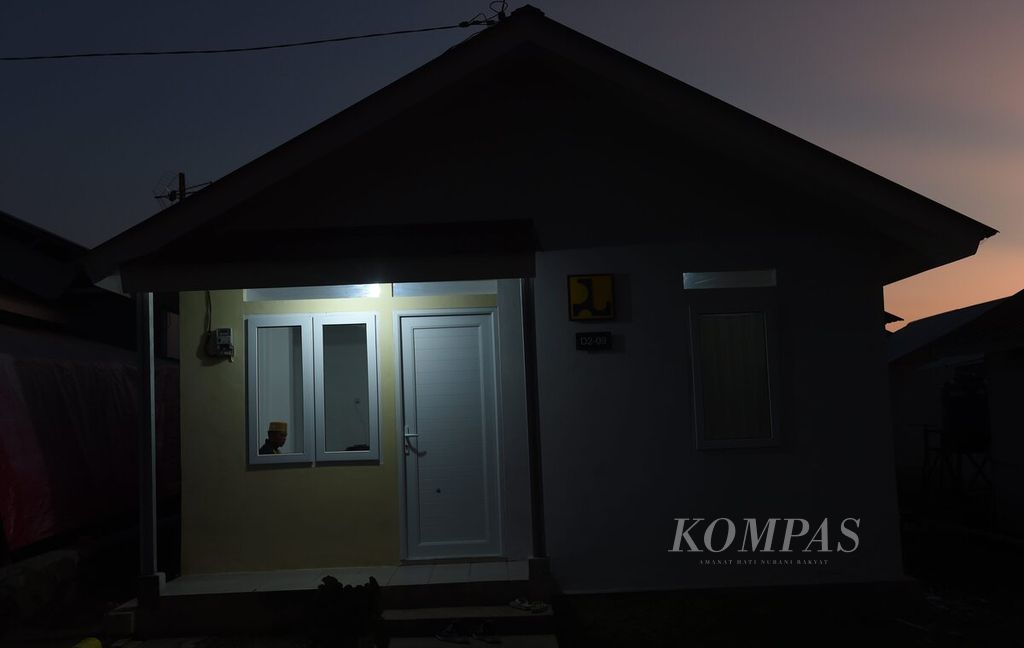 Ripin, salah satu warga hunian tetap Sumbermujur di Kecamatan Candipuro, Kabupaten Lumajang, Jawa Timur, terlihat dari jendela rumahnya, Minggu (10/7/2022) malam. Kawasan hunian ini bagian dari penanganan pascabencana erupsi Gunung Semeru. 