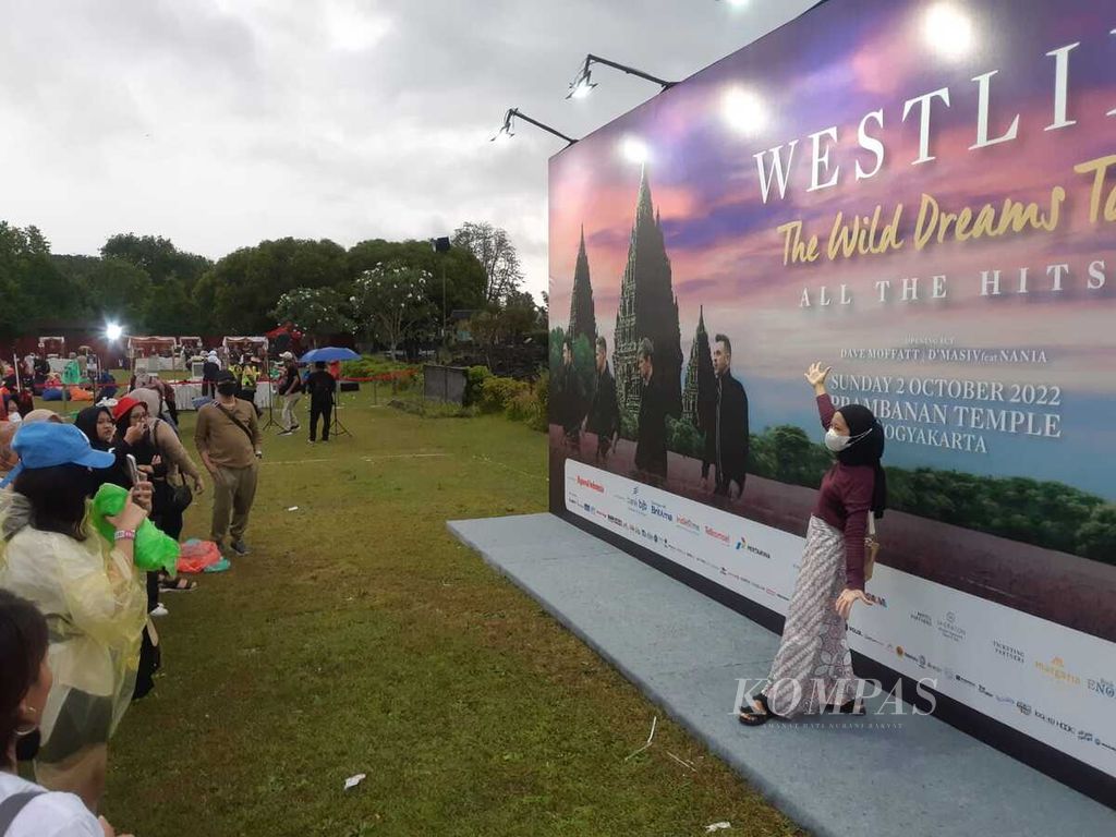 Penonton berpose di depan gambar Westlife sebelum dimulainya konser grup pria asal Irlandia itu di Lapangan Brahma, Candi Prambanan, Yogyakarta, Minggu (2/10/2022).