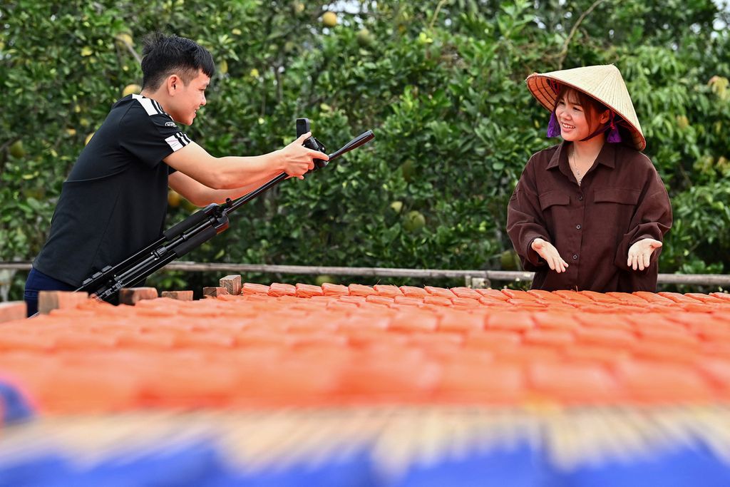 Vi Thi Anh (kanan) tengah tampil dalam tayangan langsung saat menjemur mie beras dagangannya. Kamera dipegang suaminya dalam tayangan yang diambil 7 November 2023 ini. 