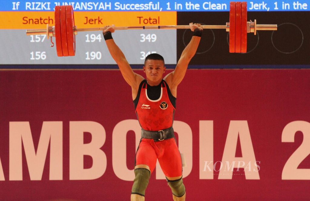 Rizki Juniansyah, lifter muda Indonesia yang masih berusia 20 tahun, mengangkat pelat-pelat besi di kategori <i>snatch </i>pada SEA Games Kamboja 2023, di National Olympic Stadium, Kamboja, Minggu (14/5/2023). Rizki masuk di kategori putra 73 kg, berbeda dengan tahun lalu saat ia mendapatkan perak di kelas 81 kg dan mendapatkan perak.