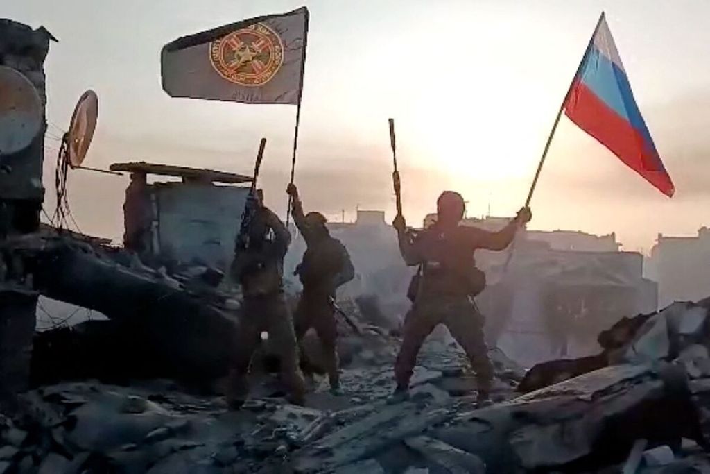 Foto hasil tangkapan gambar video yang diunggah di Telegram, Sabtu (20/5/2023), memperlihatkan pasukan bayaran asal Rusia, Wagner Group, mengibarkan bendera Rusia (kanan) dan bendera Wagner Group di atas gedung yang hancur di Bakhmut, Ukraina timur. 