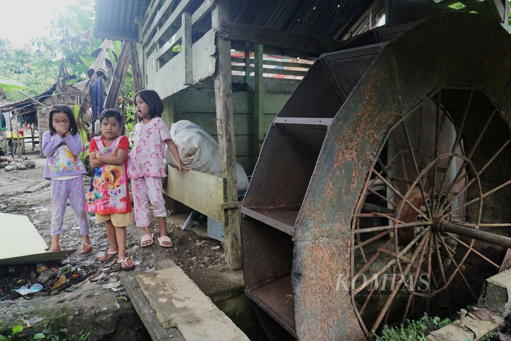 Anak-anak bermain di dekat kincir air pembangkit listrik tenaga mikrohidro (PLTMH) yang tak lagi berfungsi, Sabtu (16/7/2022), di Desa Mengkang, Kecamatan Lolayan, Bolaang Mongondow, Sulawesi Utara. Rangkaian PLTMH itu diadakan pada 2006 untuk memastikan anak-anak dapat belajar dengan baik di malam hari.