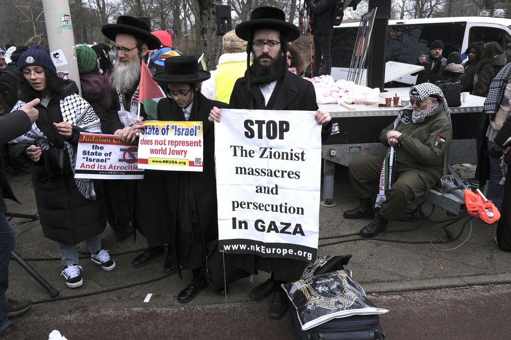 Meskipun berkostum khas Yahudi, sekelompok pengunjuk rasa memegang poster yang berisi tulisan untuk segera menghentikan serangan Israel ke Gaza selama demonstrasi di luar Mahkamah Internasional di Den Haag, Belanda, Kamis (11/1/2024). 