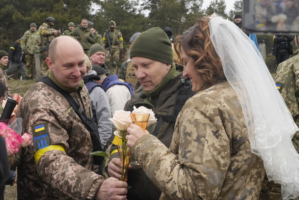  Seorang anggota Pasukan Pertahanan Teritorial Ukraina mengucapkan selamat kepada pasangan Lesia Ivashchenko (kanan) dan Valerii Fylymonov (tengah) saat upacara pernikahan mereka yang berlangsung di tengah serangan Rusia di sebuah pos pemeriksaan di Kiev, Ukraina, Minggu (6/3/2022). 