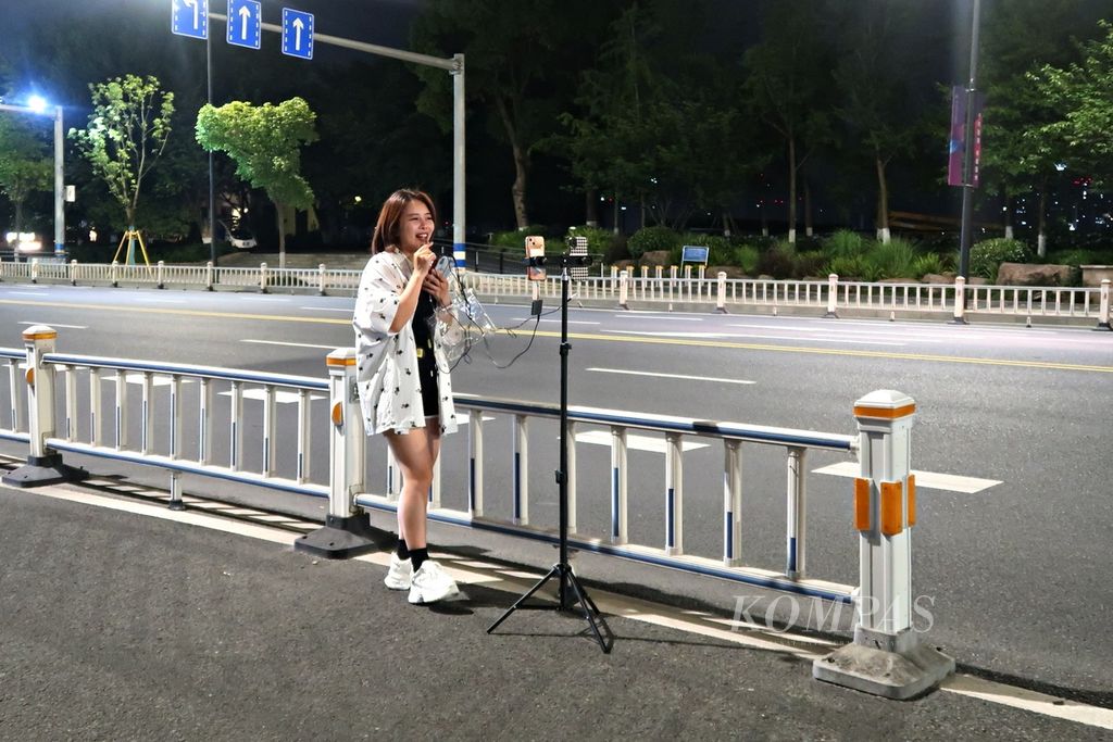 Seorang perempuan muda yang bekerja sebagai pemengaruh terlihat melakukan siaran langsung pada tengah malam untuk menyanyi kepada para pengikutnya di media sosial di salah satu jalan di Kota Wenzhou, Zhejiang, China, Senin (15/5/2023).
