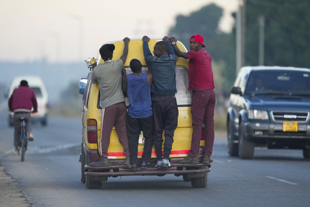 Sejumlah pria bergelantungan di bagian belakang angkutan umum di Harare, Zimbabwe, Kamis (2/6/2022). 