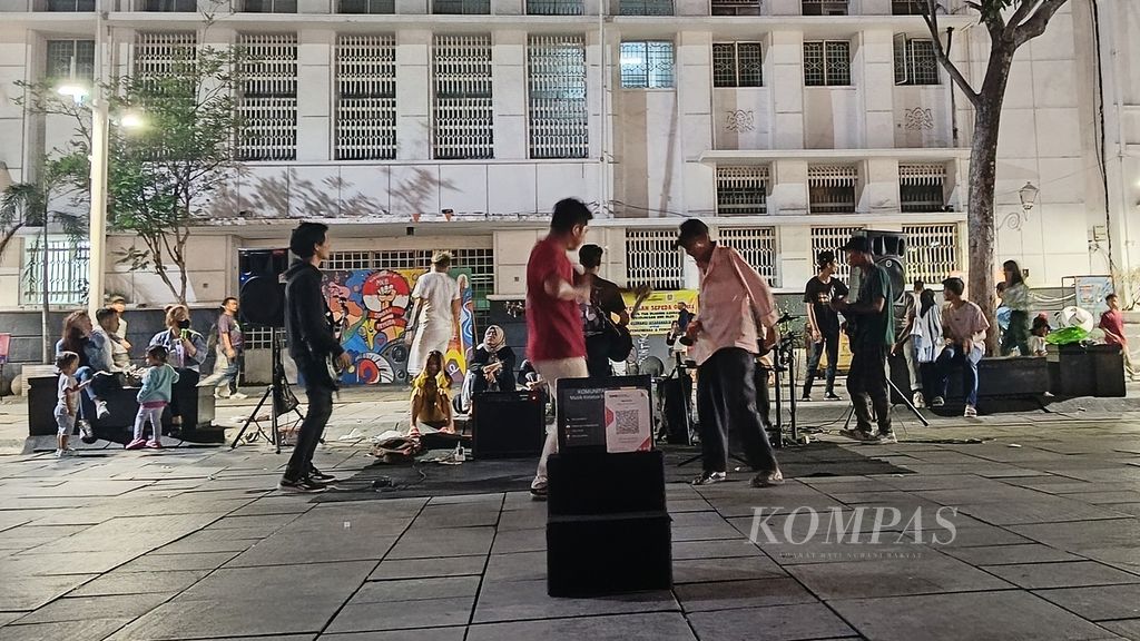 Seorang pengunjung (baju pink) ikut bergoyang di panggung jalanan Kota Tua Jakarta, Kamis (21/12/2023). Komunitas Musik KotaTua Bersatu yang digawangi Nawi itu merupakan seniman jalanan.