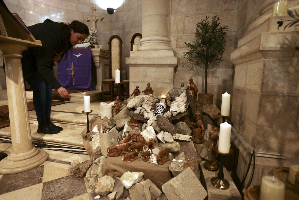  Seorang anggota jemaat menyalakan lilin di dekat dekorasi kelahiran Yesus yang tahun ini diletakkan di puing-puing perang di Gereja Evangelical Lutheran di Bethlehem, Tepi Barat, Rabu (6/12/2023).