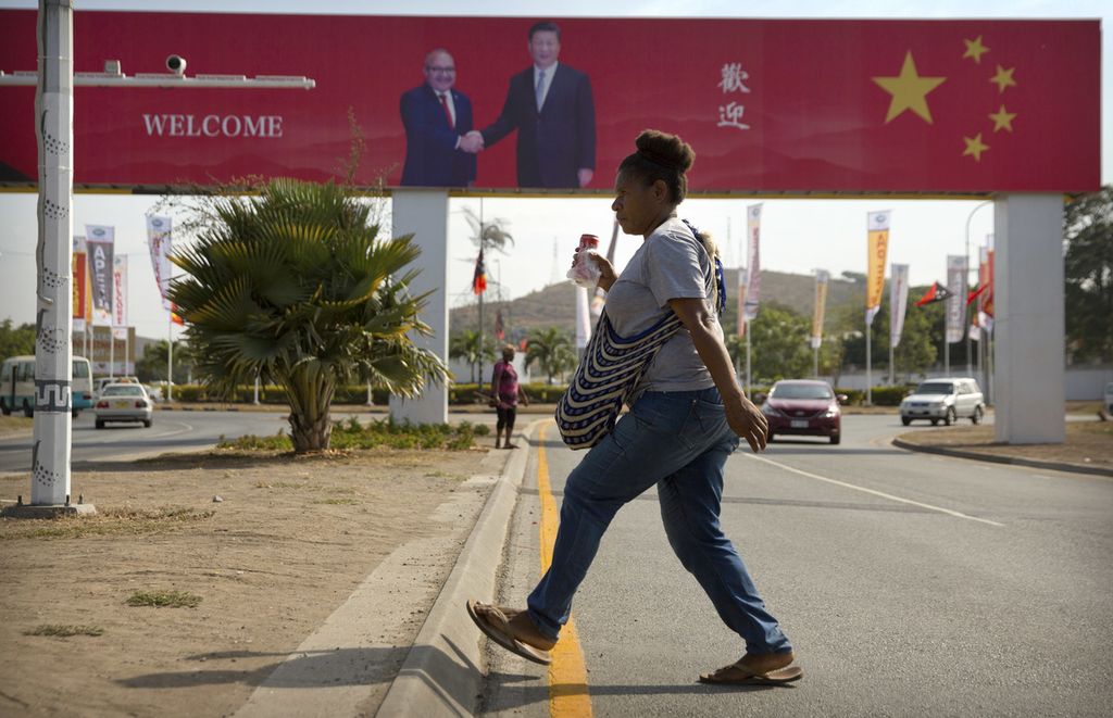 Seorang perempuan menyeberangi jalan di Port Moresby, Papua Niugini, 15 November 2018. Tampak poster Perdana Menteri PNG Peter O'Neill bersalaman dengan Presiden China Xi Jinping dalam rangka kunjungan Xi ke PNG.     