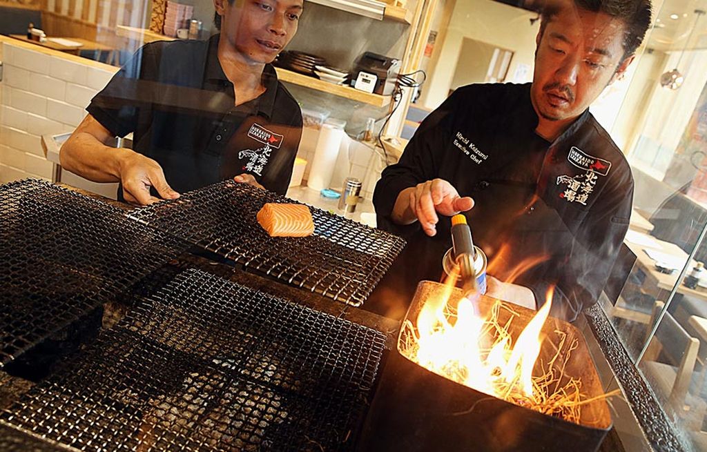 Chef Hiroshi Koizumi (kanan) menyiapkan menu daging ikan salmon yang dipanggang di atas bara jerami, di Restoran Hokkaido Izakaya Jakarta. 