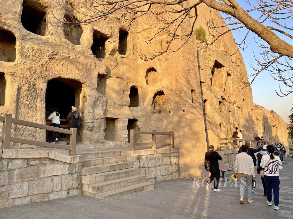 Para pengunjung mengintip ke dalam salah satu relung di dinding tebing di kompleks situs bersejarah Gua Yungang, Provinsi Shanxi, China, Sabtu (21/10/2023).