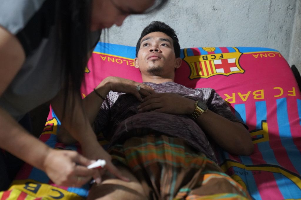 Muhammad Syafi’i (32) sedang diobati Dinda, istrinya, di rumahnya di Desa Selorejo, Kabupaten Gunung Kidul, DI Yogyakarta, Rabu (26/7/2023). Syafi,i saat ini menderita kerusakan saraf pada bagian tubuhnya imbas dari kecelakaan kerja yang dia alami ketika menjadi anak buah kapal migran di kapal China pada pertengahan tahun 2021 silam. Dalam kecelakaan kerja itu, Syafi’i mengalami luka bakar serius karena ketumpahan minyak mendidih.
