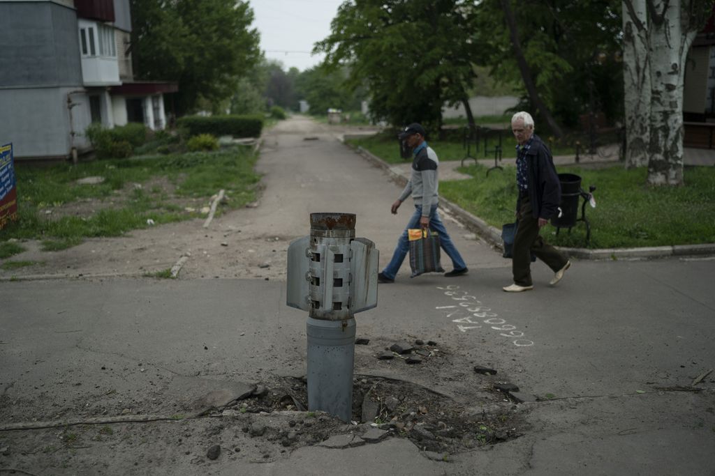 Dua warga berjalan melewati sisa roket yang tertancap di jalan di Lysychansk, wilayah Lugansk, Ukraina, 13 Mei 2022. 