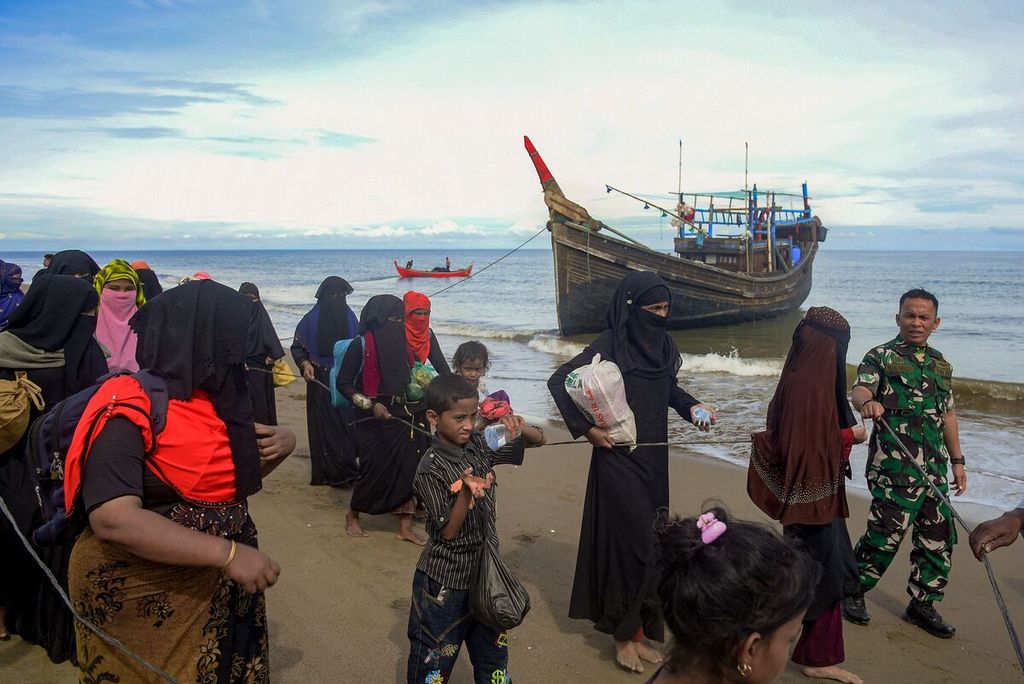 Pengungsi Rohingya dipandu oleh seorang tentara berjalan di pesisir Bluka Teubai, Aceh Utara, setelah kapal yang mereka tumpangi terdampar di pantai utara Aceh. Kapal itu mengangkut 119 pengungsi.
