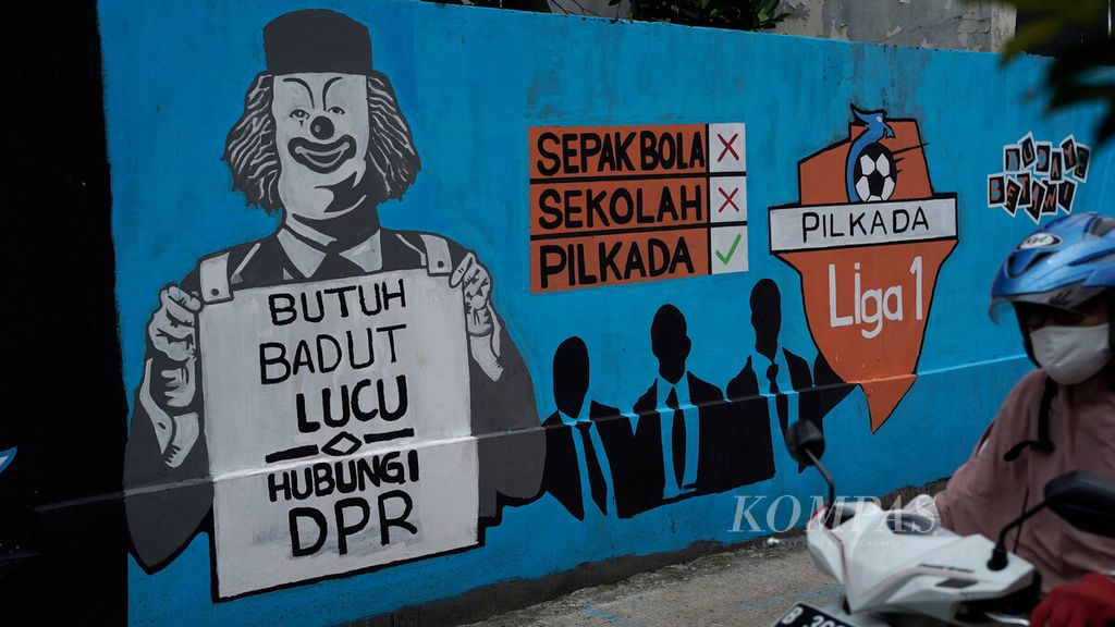 Warga melintasi jalan di sekitar mural Covid-19 dan politik di Jatikramat, Kota Bekasi, Jawa Barat, Senin (26/10/2020). Saat itu sikap elite politik yang memperbolehkan pilkada dalam pandemi Covid-19 dikritik karena dinilai bertentangan dengan protokol kesehatan.