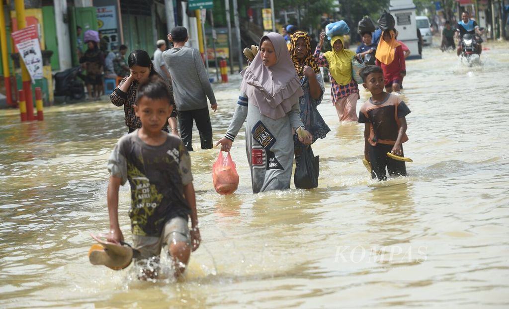 Dengan membawa barang belanjaan setelah dari pasar, warga melintasi banjir di Jalan Imam Bonjol, Kecamatan Sampang, Kabupaten Sampang, Jawa Timur, Senin (2/1/2023). 