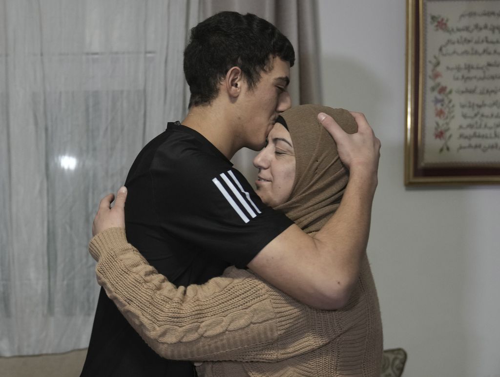 Muhammad Abu Al-Humus (kiri) memeluk ibunya saat keduanya bertemu di rumah di kawasan Issawiya, Jerusalem, Selasa (28/11/2023). Kelompok Hamas kembali membuka peluang untuk bertukar tawanan dan memperpanjang jeda pertempuran dengan Israel.  
