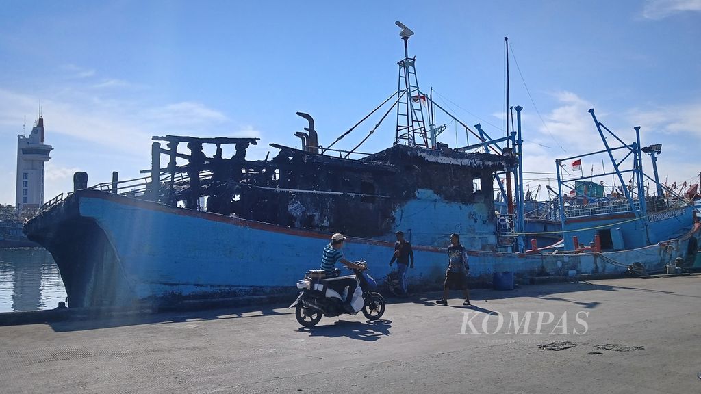 Warga dan pekerja melintas di sekitar salah satu kapal yang terbakar, Kamis (21/3/2024). Dua kapal ikan yang bersandar di Pelabuhan Muara Baru, Penjaringan, Jakarta Utara, terbakar pada Rabu (20/3/2024) sore.