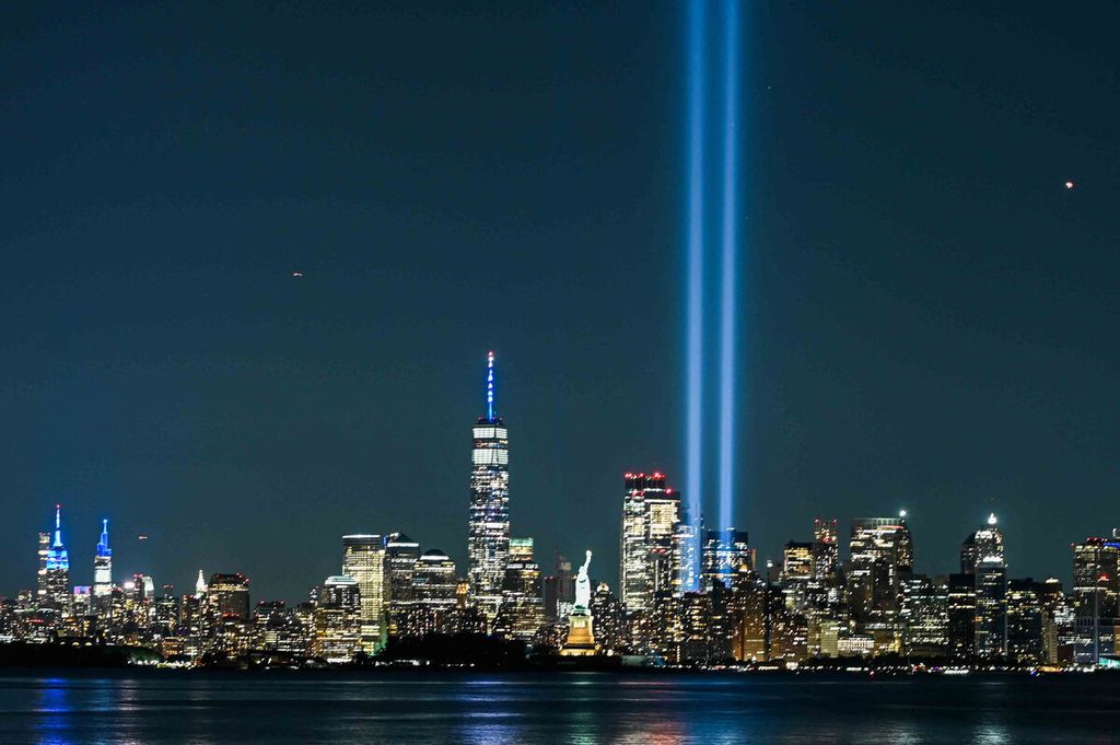 Patung Liberty bersinar di dekat sorotan cahaya penghormatan sebagai bagian dari peringatan 20 tahun serangan teroris di New York, AS, Sabtu (11/9/2021). 