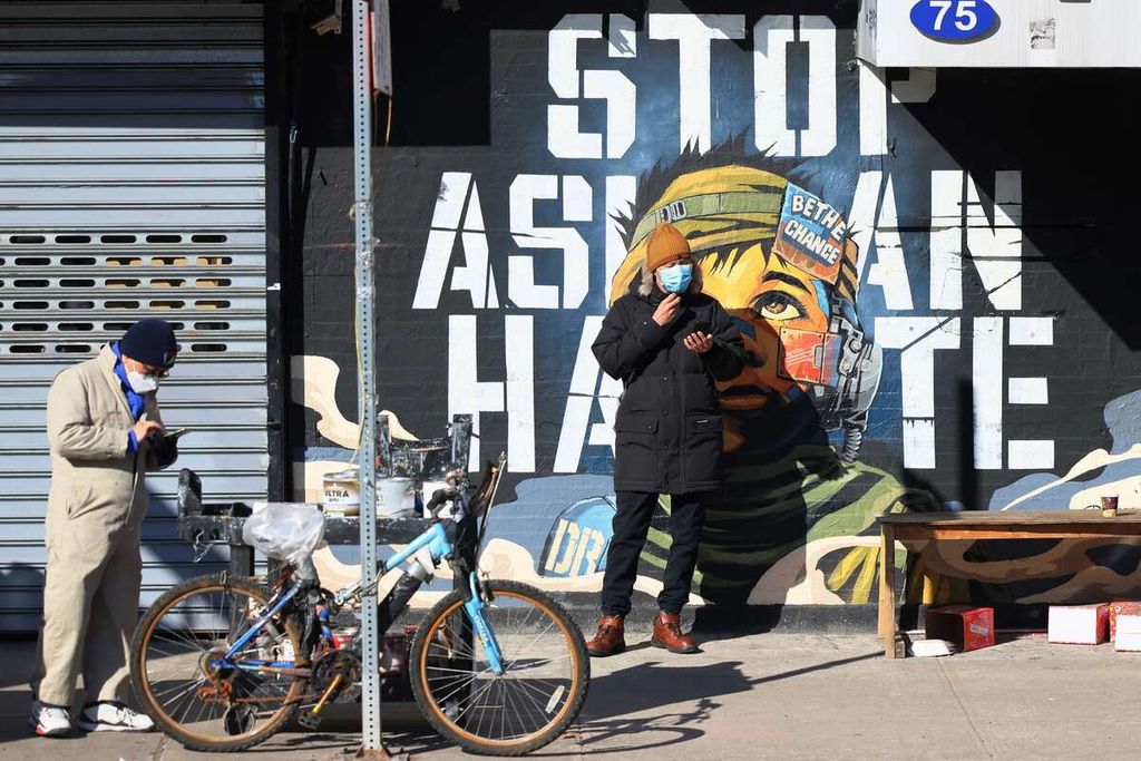 Dua orang warga berdiri di depan mural bertuliskan "Stop Asian Hate" atau "Hentikan Tindak Kebencian pada Warga Asia" di sebuah dinding di Kota New York. Foto diambil pada Senin (14/2/2022) saat terjadi unjuk rasa memprotes kekerasan terhadap warga keturunan Asia. 