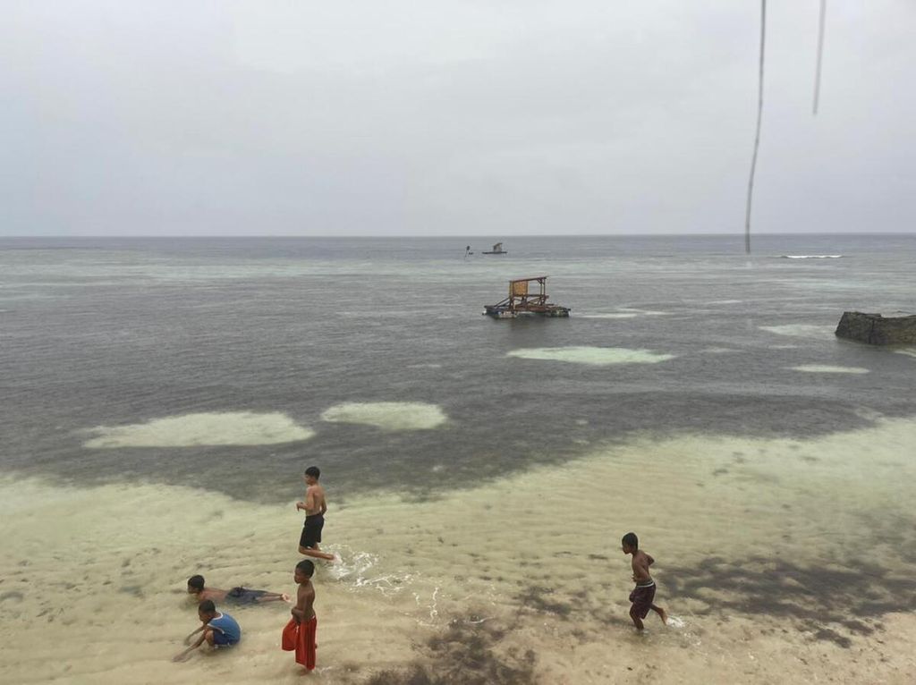 Di bawah guyuran hujan, anak-anak bermain di tepian Pantai Sombu, Wangi-wangi, Wakatobi, Sulawesi Tenggara, seiring cuaca yang tidak menentu, Kamis (23/6/2022). Gelombang hingga 4 meter berpotensi terjadi di wilayah Wakatobi dan perairan sisi timur Laut Banda.