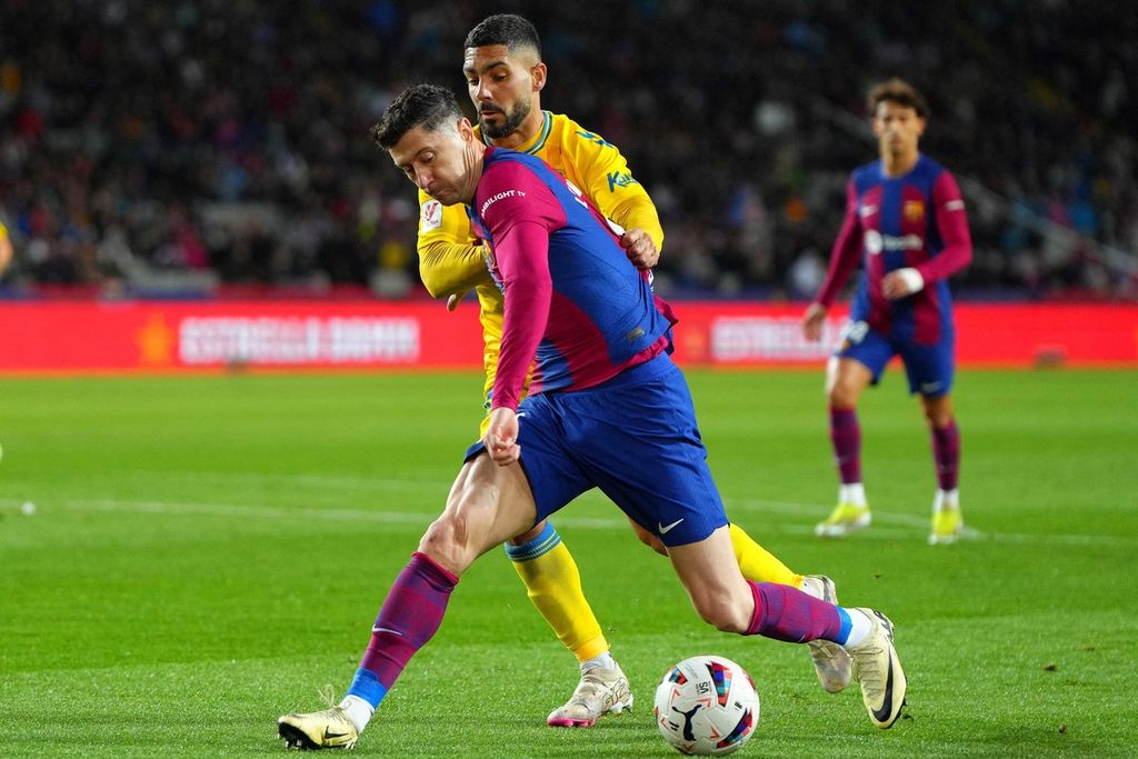 Penyerang Barcelona, Robert Lewandowski, berebut bola dengan bek Las Palmas, Alex Suarez, dalam pertandingan Liga Spanyol antara Barcelona dan Las Palmas di Stadion Olimpiade Lluis Companys, Barcelona, Minggu (31/3/2024) dini hari WIB. 