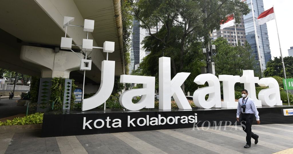 Pekerja kantoran berjalan melewati logo Jakarta Kota Kolaborasi di Jalan Sudirman, Jakarta, Selasa (25/1/2022). 