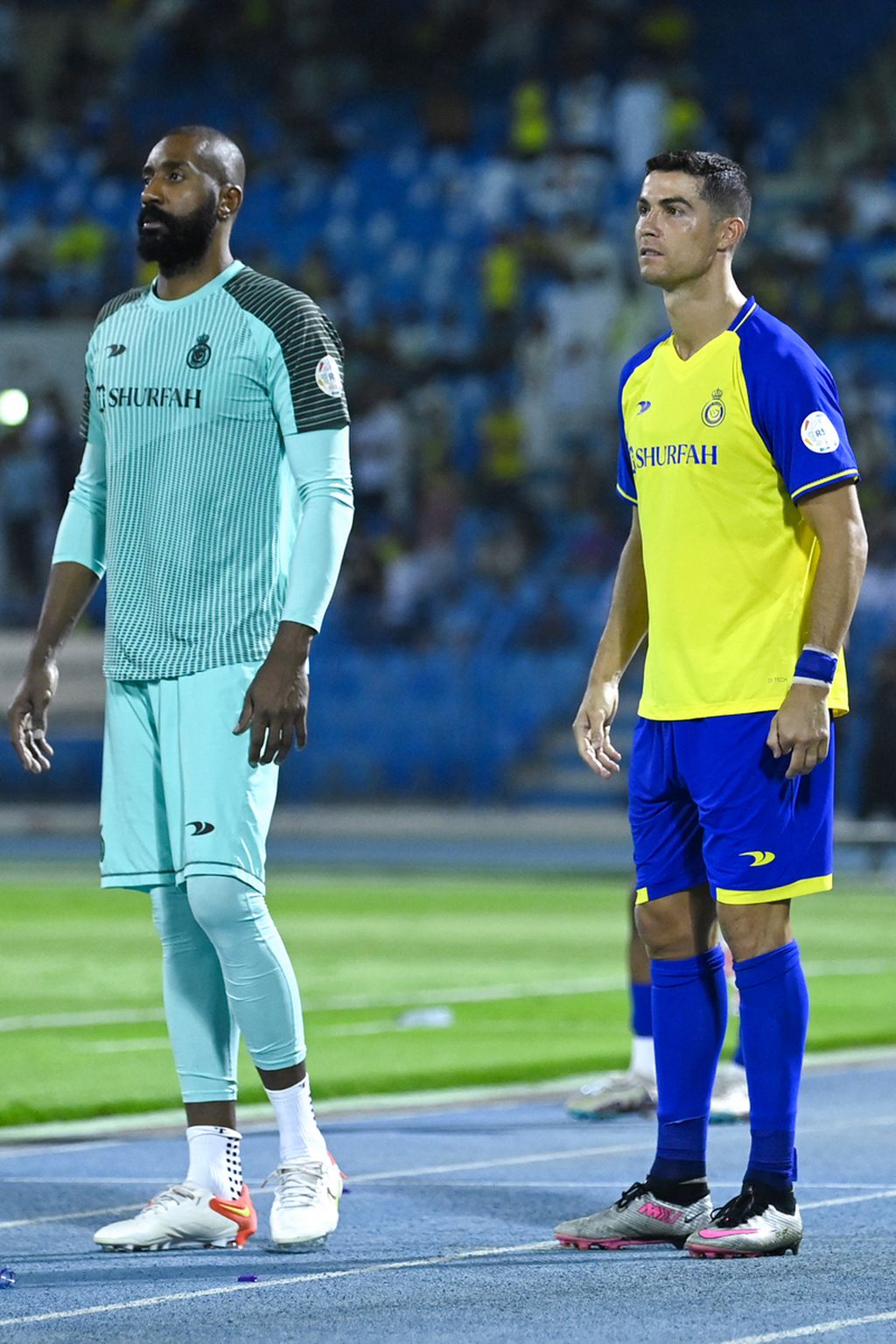 Cristiano Ronaldo berdiri di sisi lapangan bersama rekannya, kiper Al-Nassr, Waleed Abdullah, di pengujung laga menghadapi Ettifaq di Stadion Pangeran Mohammed bin Fahd jelang laga melawan Ettifaq, Minggu (28/5/2023) dini hari WIB. 