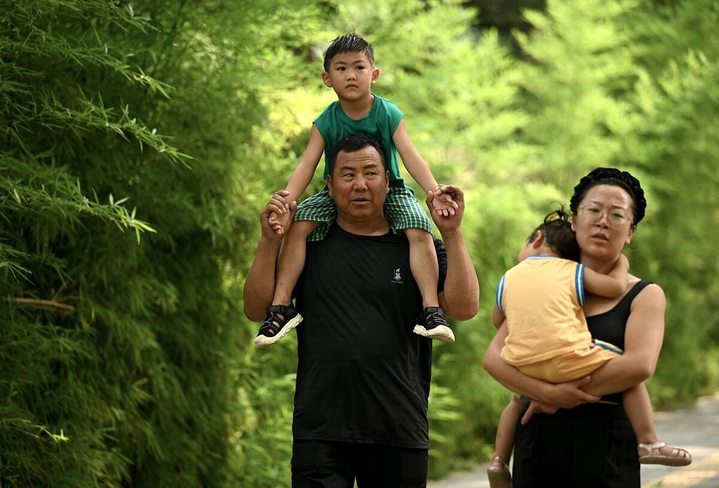Orangtua menggendong anak-anak mereka di Beijing, 2 Agustus 2022. Populasi China akan mulai menurun pada 2025 karena keluarga semakin mengecil dan warga lansia semakin banyak. 
