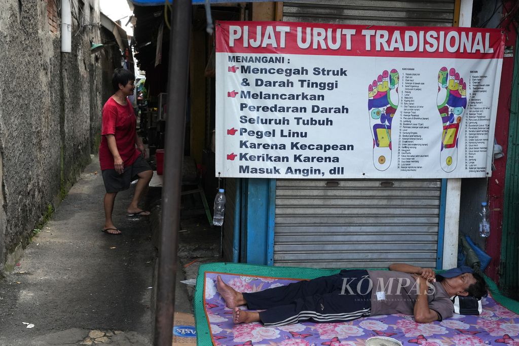 Tukang pijat terlelap di depan pertokoan di Jalan Bekasi Barat, Kelurahan Rawa Bunga, Jatinegara, Jakarta Timur, Sabtu (20/4/2024). Lapak penjual di trotoar dan pertokoan lama kini bernasib sama, sepi pembeli, dan hanya bisa bertahan.  