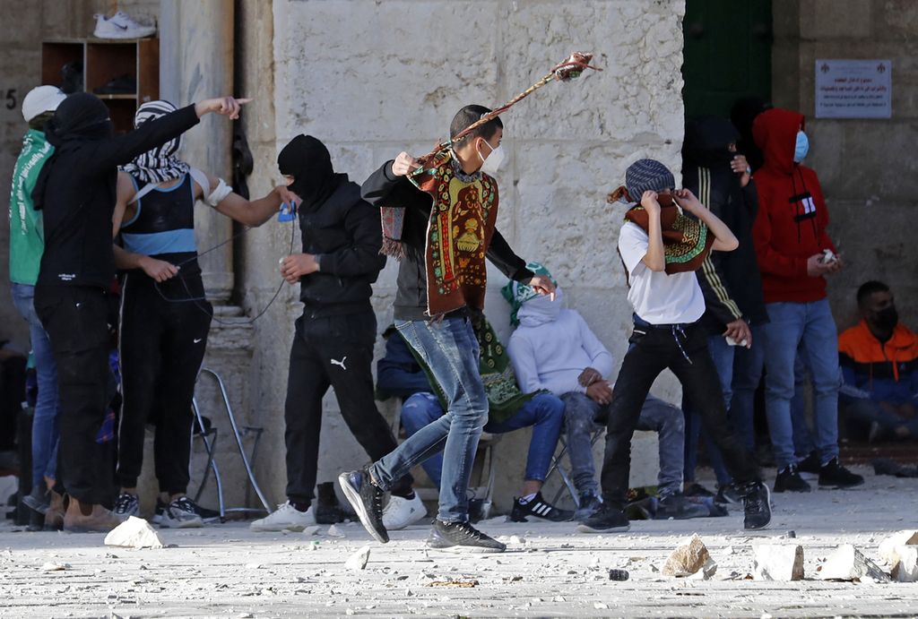 Sejumlah pemuda Palestina melempari aparat keamanan Israel dengan batu ketika kedua pihak bentrok, Jumat (22/4/2022). Liga Arab mengecam tindakan aparat keamanan Israel yang mengizinkan warga Yahudi beribadah di kompleks Masjid Al Aqsa sebagai tindakan yang provokatif dan ilegal. 