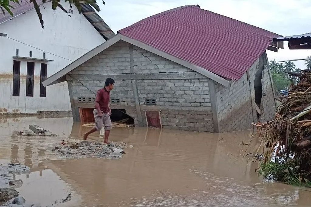 Warga melintas di depan rumah di Desa Torue, Kecamatan Torue, Kabupaten Parigi Moutong, Sulteng, Jumat (29/7/2022), yang diterjang banjir bandang pada Kamis (28/7/2022). Banjir bandang tersebut menewaskan tiga orang, empat orang lainnya masih dicari.