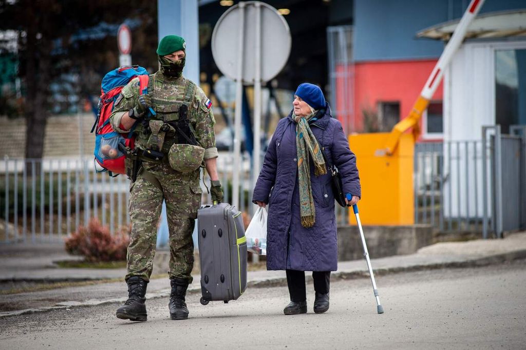 Seorang tentara Slowakia membantu seorang wanita Ukraina membawa barang bawaannya saat melintasi perbatasan di Vysne Nemecke, Slowakia timur, pada 26 Februari 2022, dua hari setelah Rusia menginvasi Ukraina.