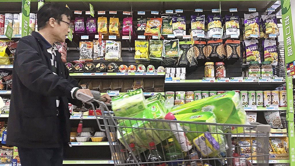 Seorang warga  Beijing mendorong kereta belanja melewati pajangan makanan kaleng yang diimpor dari Amerika Serikat dan negara-negara lain di sebuah supermarket di Beijing, Senin (2/4/2018). Menyikapi kebijakan tarif yang diterapkan AS, China menaikkan bea impor pada sejumlah produk AS, seperti produk daging,  buah, dan kacang-kacangan. 