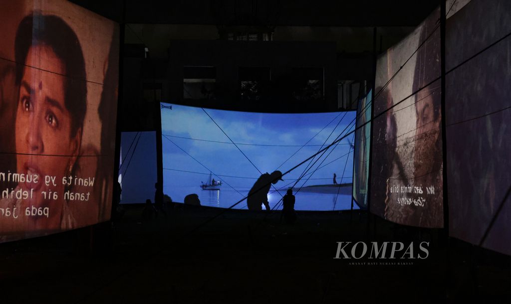 Siluet warga melintas di layar yang tengah memutar film dalam festival layar tancap di Lapangan Babakan, Kecamatan Setu, Tangerang Selatan, Banten, Rabu (18/1/2023) malam.