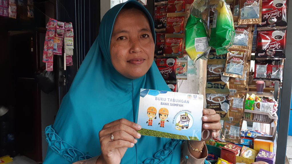 Indrawati (44), anggota Bank Sampah Kenanga, menunjukkan buku tabungan sampah di warungnya di RT 015 RW 004, Kelurahan Semper Barat, Cilincing, Jakarta Utara, Kamis (27/7/2023). Ia juga menjadi salah satu pemilik warung yang menerima fasilitas pinjaman usaha dari Bank Sampah Kenanga.