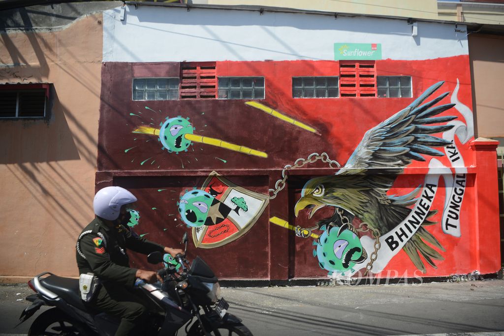 Personel militer melintas di depan mural di kawasan Keprabon, Banjarsari, Surakarta, Jawa Tengah, Jumat (10/9/2021). Melalui mural tersebut, masyarakat diajak untuk optimistis melawan pandemi dengan bekal semangat persatuan bangsa.