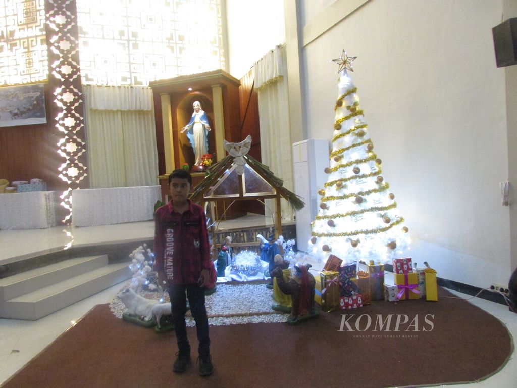 Aleks (12) berfoto dengan latar pohon natal atau kandang natal seusai misa II malam Natal di Gereja Paroki Penfui, Kupang, NTT, Jumat (24/12/2022). 