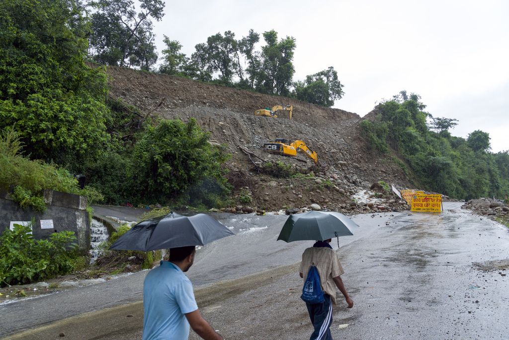 Warga berjalan di tengah hujan dekat jalan raya yang tertutup tanah longsor di Dharamshala, India, 14 Agustus 2023. Hujan deras memicu banjir dan tanah longsor di wilayah Pegunungan Himalaya dan menewaskan sedikitnya 26 orang. 