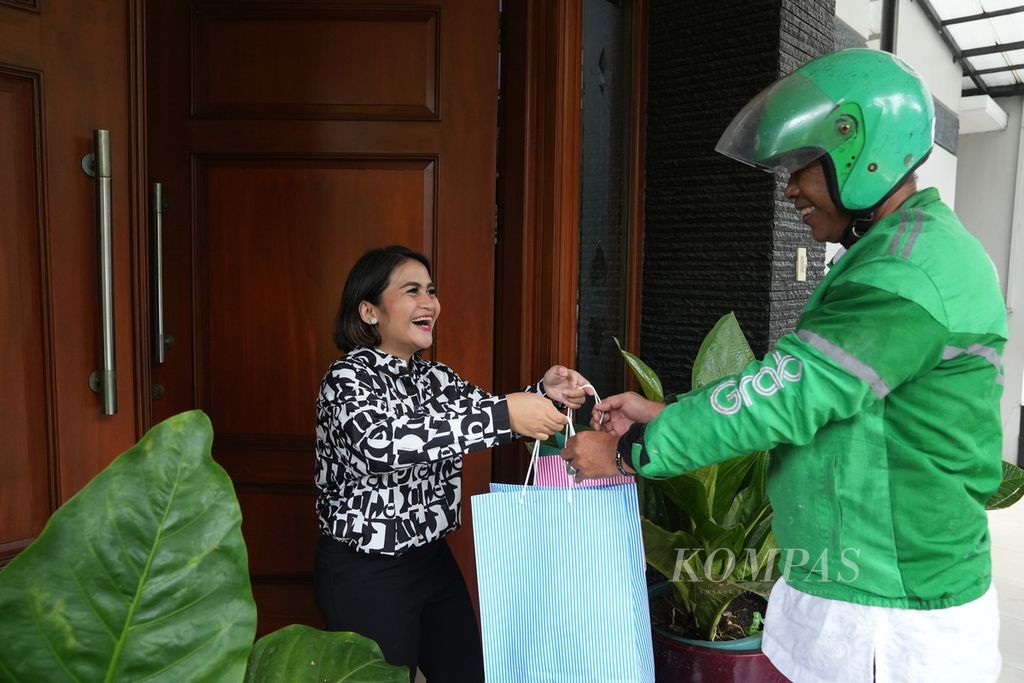 Cecille memberikan paket kue kering Cecille’s Cakes and Cookies kepada ojek daring yang akan mengantarkannya kepada pembeli di Rempoa, Tangerang Selatan, Banten, Jumat (22/3/2024). Usaha rumahan ini dirintis oleh ibunya sejak tahun 1990. 