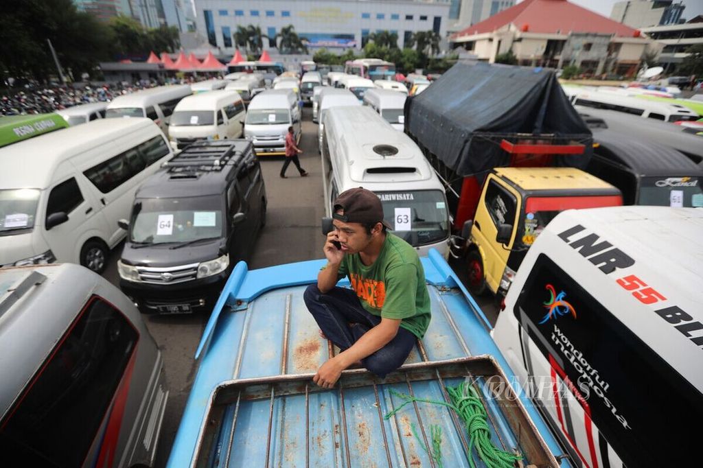 Awak kendaraan yang terjaring dalam operasi penyekatan menelepon dari atas atap mobil di area penyitaan barang bukti halaman Polda Metro Jaya, Jakarta Selatan, Senin (11/5/2020). Tiga hari operasi, 8-10 Mei, Polda Metro Jaya menyita 202 kendaraan travel gelap yang mengangkut 1.113 pemudik ke luar Jakarta. 