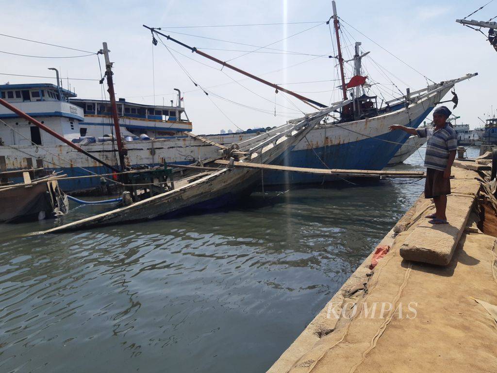 Salah satu anak buah kapal menunjuk ke arah kapal yang karam di Pelabuhan Sunda Kelapa, Jakarta Utara, Selasa (11/7/2023). Kapal yang karam sejak Mei 2023 itu mengganggu lalu lintas pelayaran pinisi.