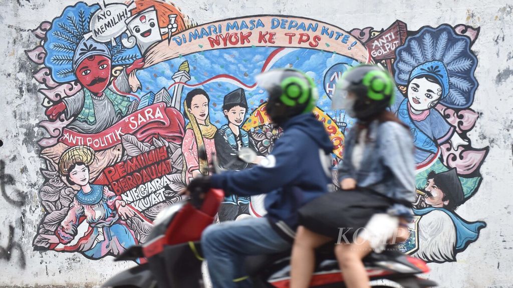 Pengendara sepeda motor melintasi mural kampanye anti-SARA dalam pemilihan umum yang tergambar di dinding jalan kawasan Dukuh Atas, Jakarta, Jumat (19/6/2020).