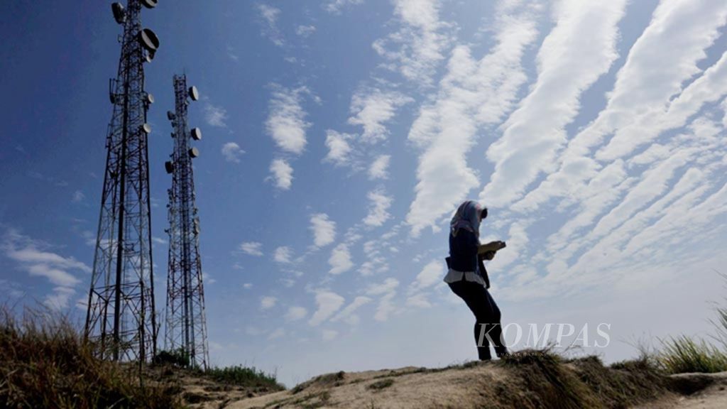 Ilustrasi.  Warga menggunakan telepon seluler di dekat menara <i>base transceiver station</i> (BTS) di kawasan Blang Panyang, Lhokseumawe, Aceh, beberapa waktu lalu.