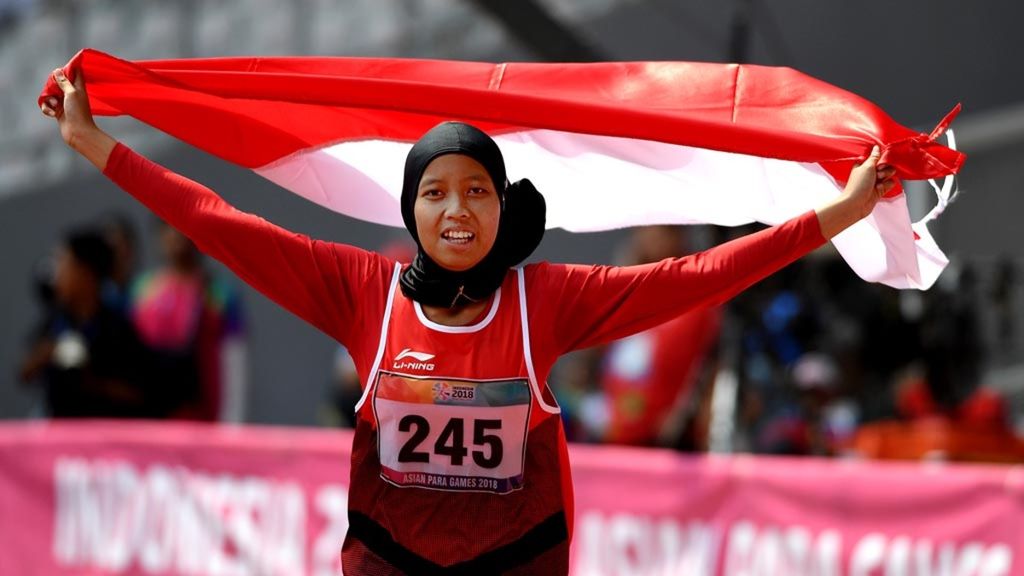 Sprinter Indonesia, Karisma Evi Tiarani, mengibarkan bendera Merah Putih seusai finis terdepan dalam nomor 100 meter putri T42 dan T63 Asian Para Games 2018 di Stadion Utama Gelora Bung Karno, Jakarta, Rabu (10/10/2018).